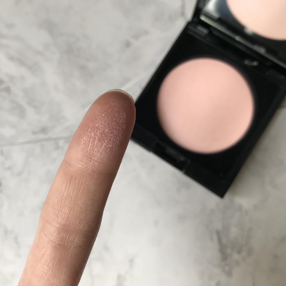アディクション スキンリフレクトセッティングパウダー 002 Translucent Pinkを指に取って粉質を見せています。